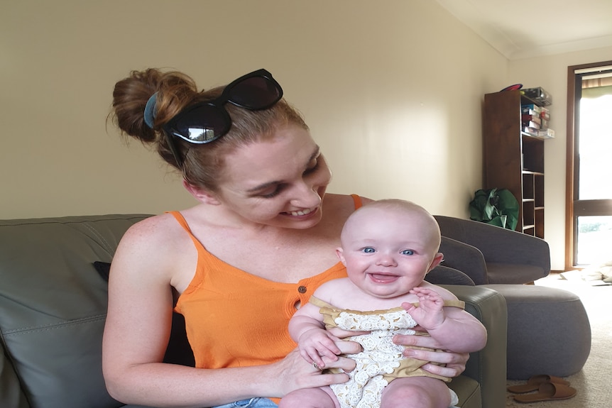 Young mum holding her baby on her lap and smiling. 