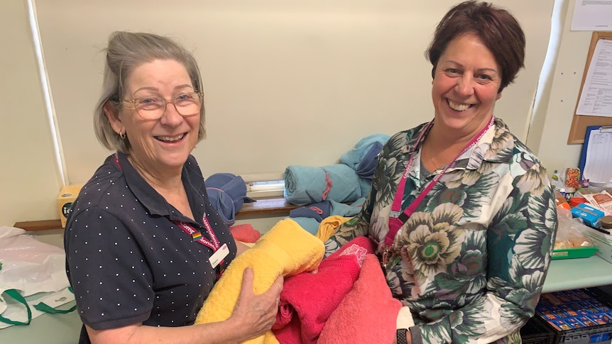 Uniting volunteer Sharon Martin and  Emergency Relief Coordinator Catherine Byrne hold donated towels in an office space. 