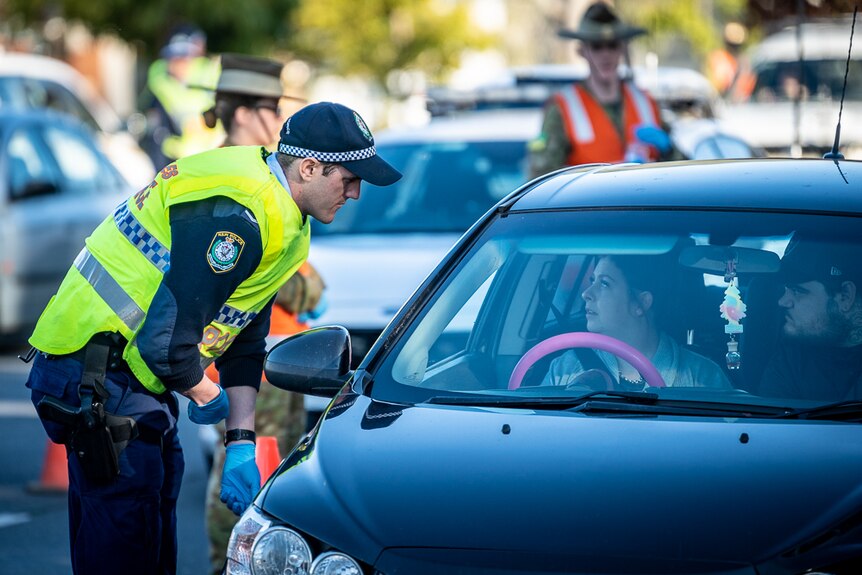 NSW police officers and a solider checking a queue of cars at border.