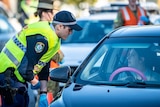 police officers and a solider checking a queue of cars