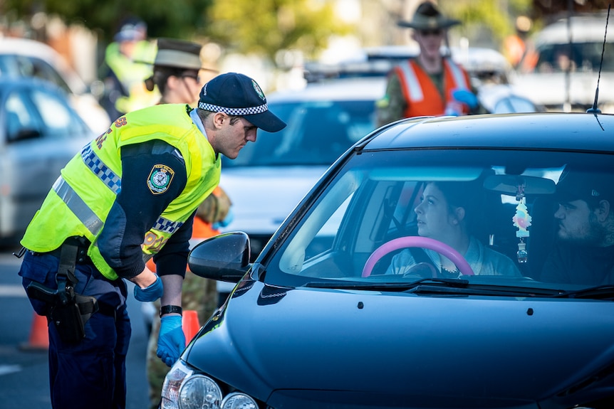 police officers and a solider checking a queue of cars