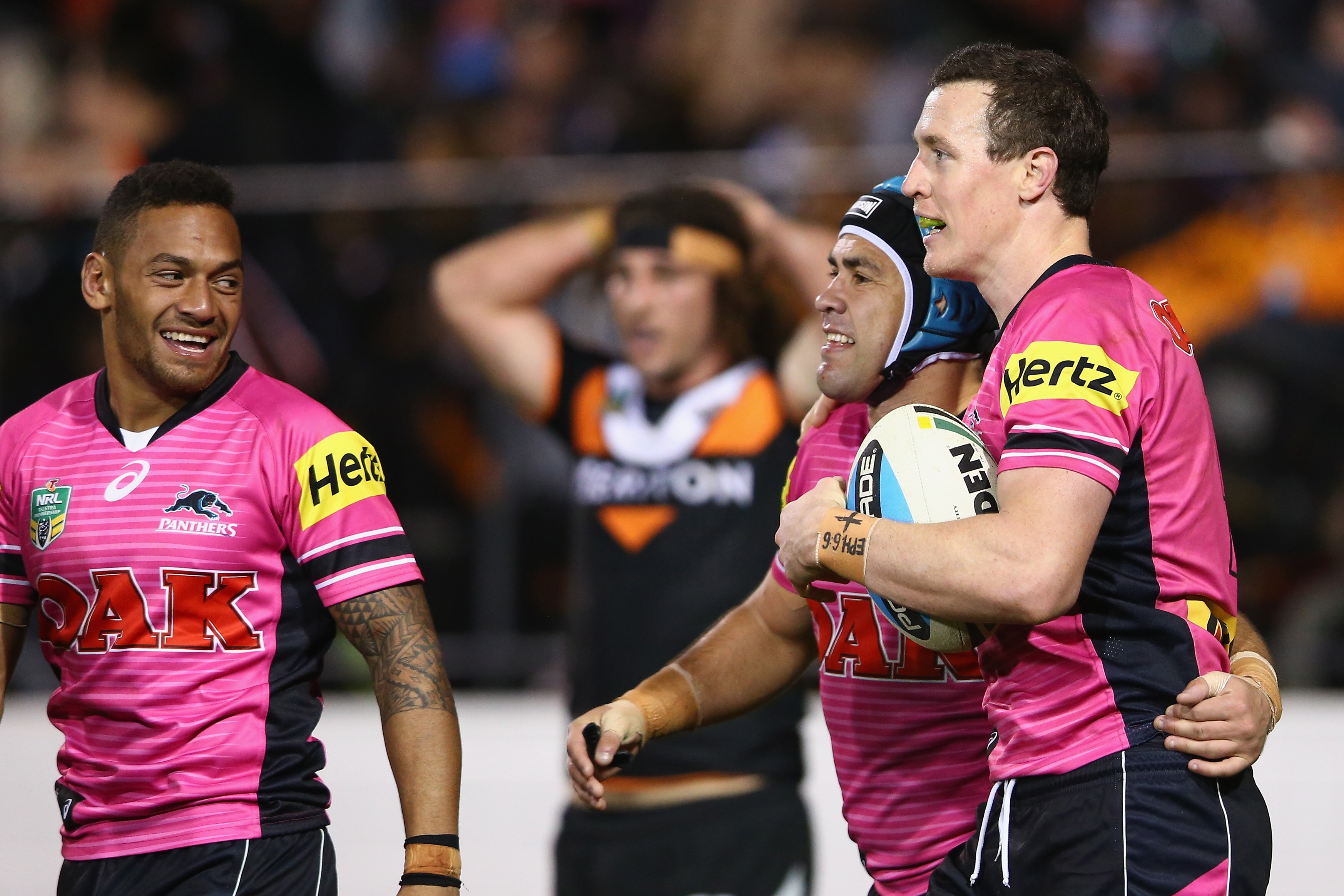 A man looks on as two teammates celebrate a try during a rugby league match