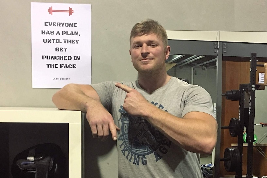 A man leans on a shelf and points to a sign at the Lads Society clubhouse