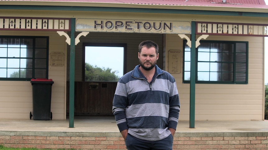 He stands in front of a sign saying 'Hopetoun' 