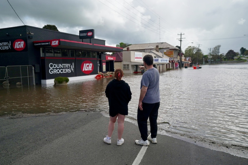 couple stand at the edge of floodwater in small victorian town with backs turned to camera