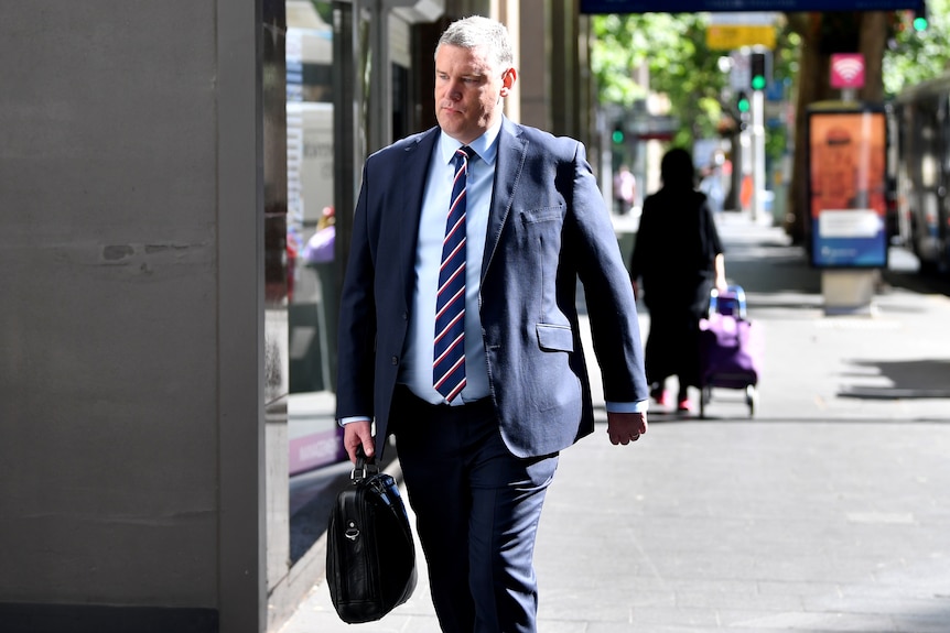 a man in a suit and tie carrying a bag walking into a building