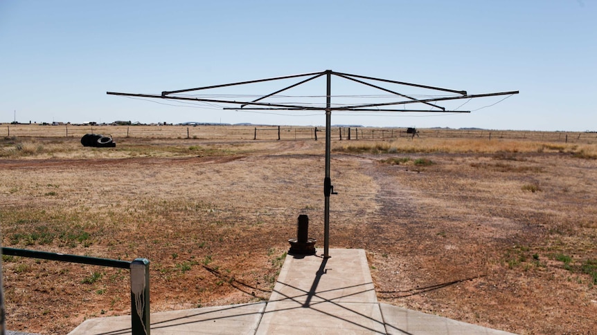 A hills-hoist clothes line in a dry backyard, opening on to drought stricken paddocks.