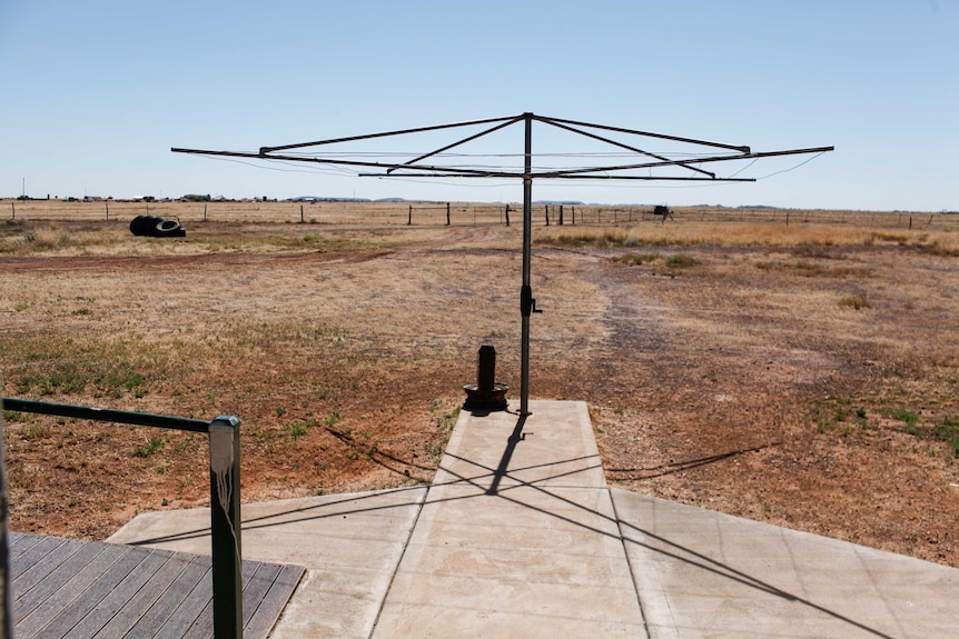 A hills-hoist clothes line in a dry backyard, opening on to drought stricken paddocks.
