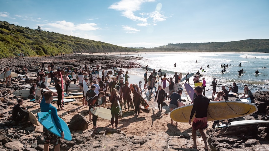 Surfers walk to the water to participate in the paddle out