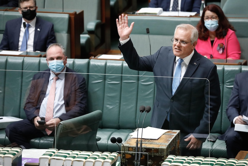 Barnaby Joyce sitting on a parliament bench, wearing a mask, while Scott Morrison stands with a hand in the air, speaking.