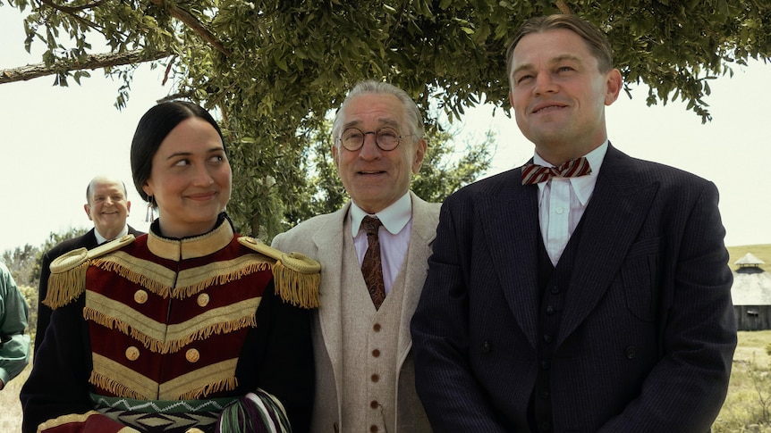 Leonardo DiCaprio, Lily Gladstone and Robert De Niro stand side-by-side in characters of Killers of the Moon film