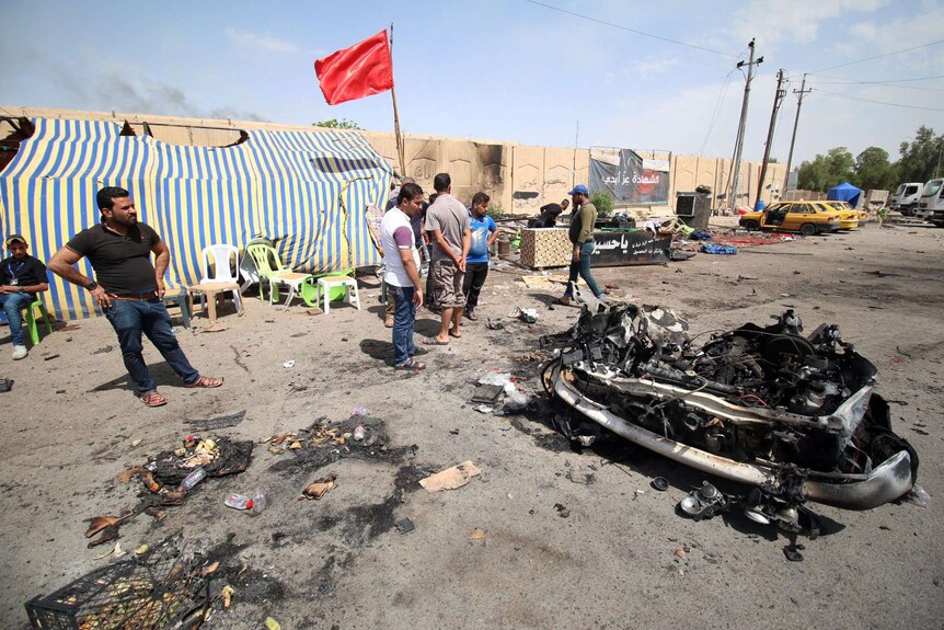 People looking at a mangled car after a bombing.