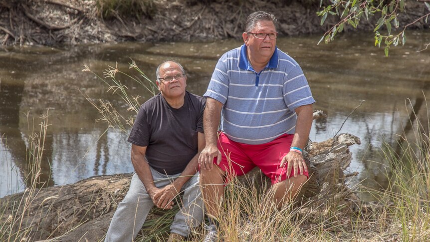 Two men sitting on a log by a river