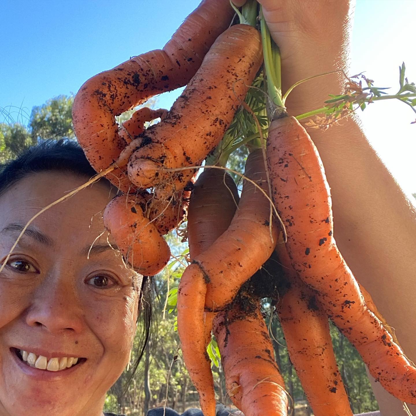 a selfie of a woman with carrots from her vegetable garden 