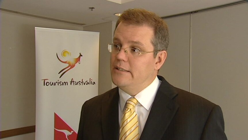 Scott Morrison giving a television interview with signage in the background showing logos of Tourism Australia and Qantas