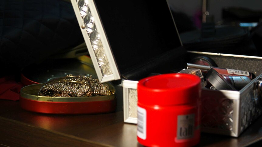 A photo of some hair gel, out of focus, and some shiny jewellery in a jewellery box.