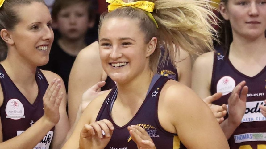 A young netballer smiles surrounded by teammates.