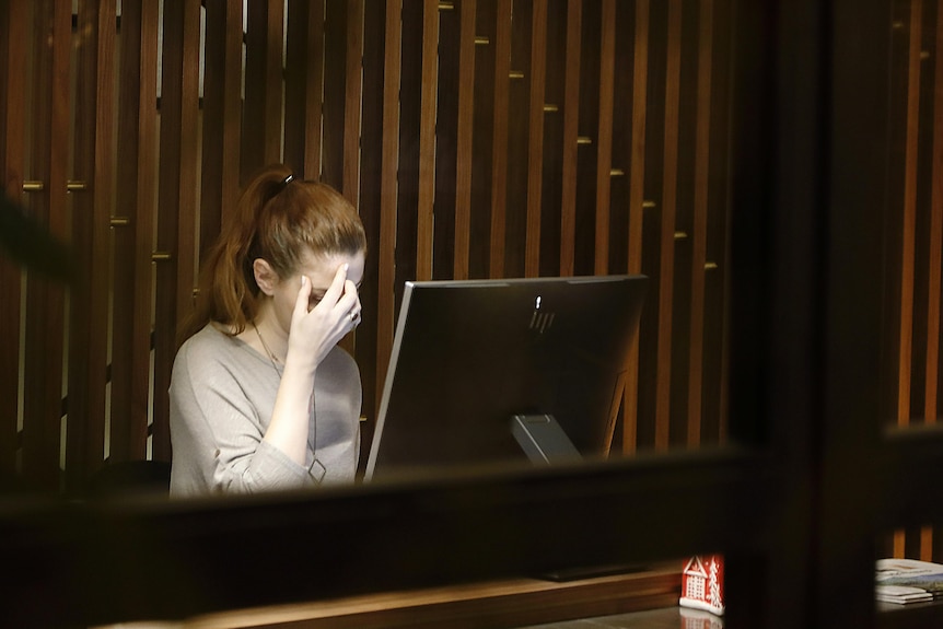 A woman with her head in her hand in front of a computer screen. 