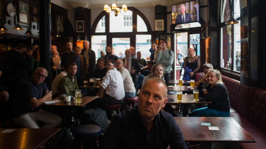 People in a London pub watch the TV with Charles III speaking.