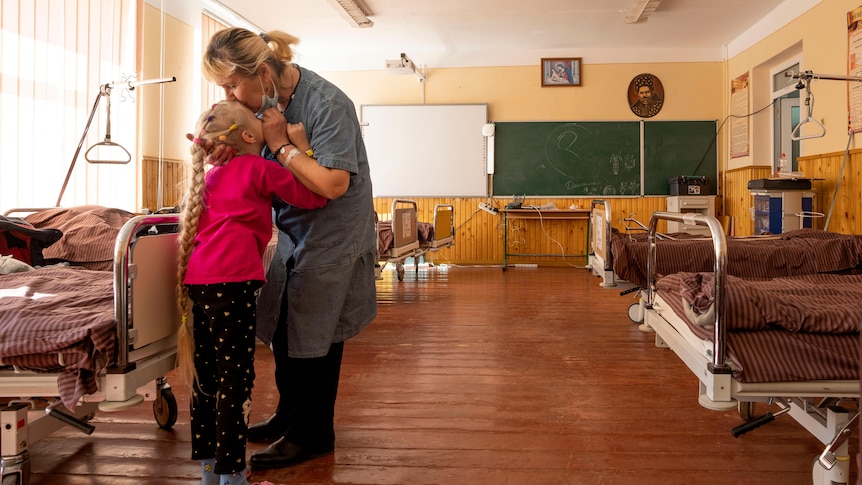 Woman kisses her 10-year-old granddaughter in a room at a school filled with beds in western Ukraine
