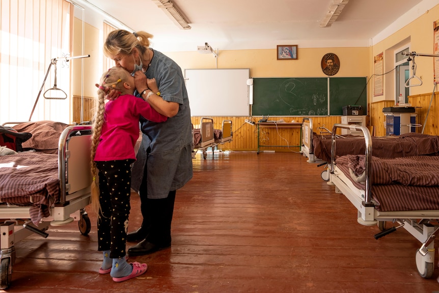Woman kisses her 10-year-old granddaughter in a room at a school filled with beds in western Ukraine