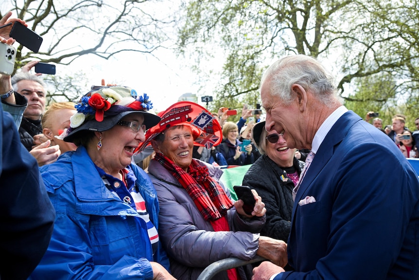 King Charles shakes the hands of two older women among a crowd of royal enthusiasts.