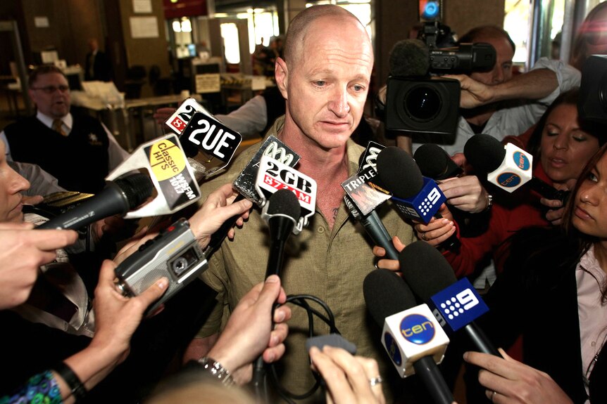 A man is surrounded by journalists with microphones and cameras.