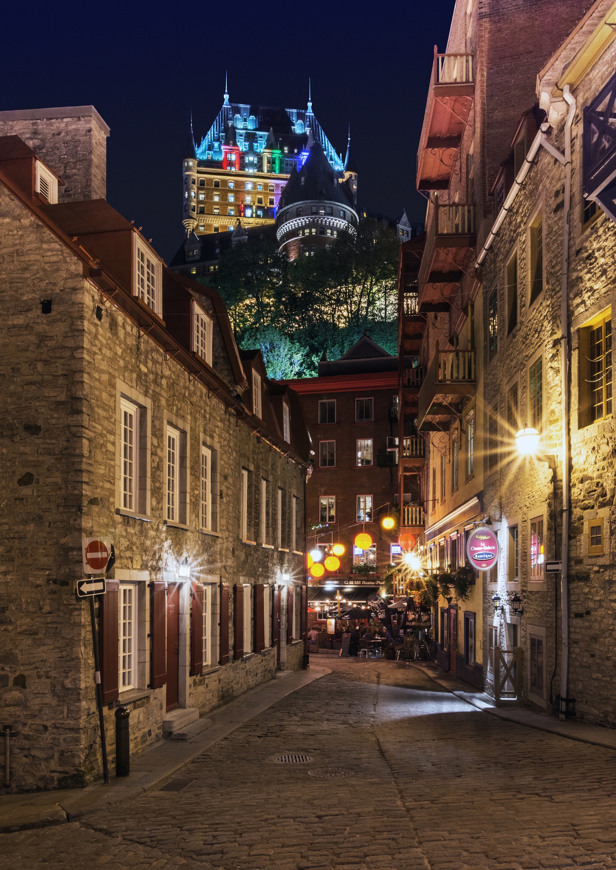 a historic, warmly lit street in Old Québec with the iconic Château Frontenac rising above