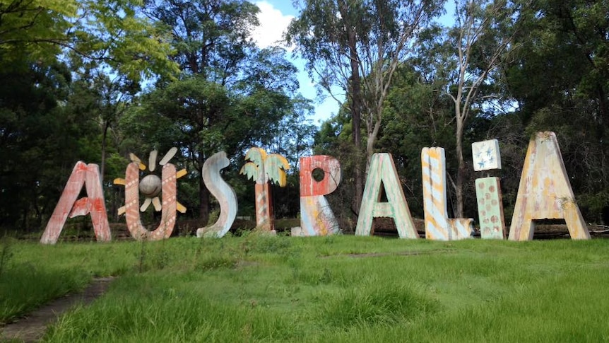 A large metal sign spelling out 'Australia' sitting in a paddock of green grass surrounded by trees.