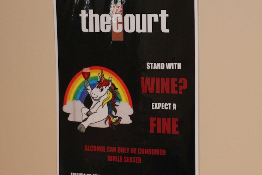 A poster shows a seated unicorn in front of a rainbow holding a glass of wine, and says 'stand with wine, expect a fine'.
