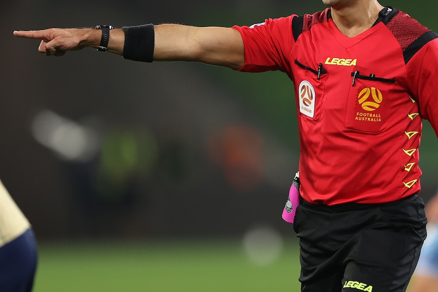 A referee points his arm wearing a red kit