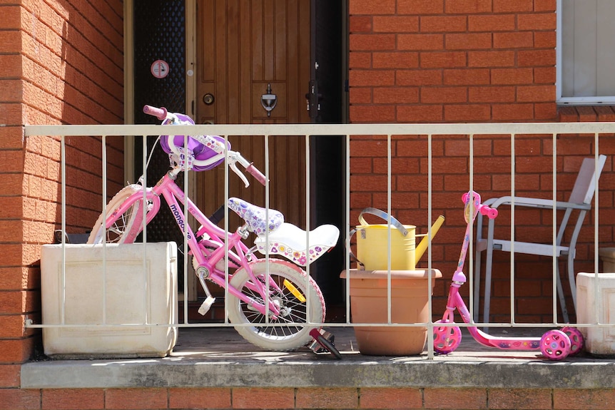 Two pink kids' bikes by the front door, which has been damaged by bullets.