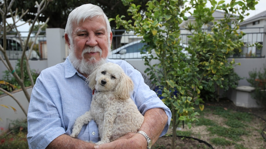 A man stands holding a small white dog in his arms.
