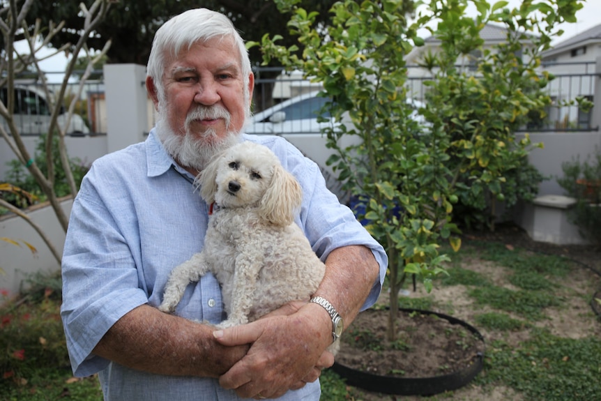 A man stands holding a small white dog in his arms.