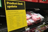A yellow and black sign hangs in front of the meat section in a supermarket, with products behind.