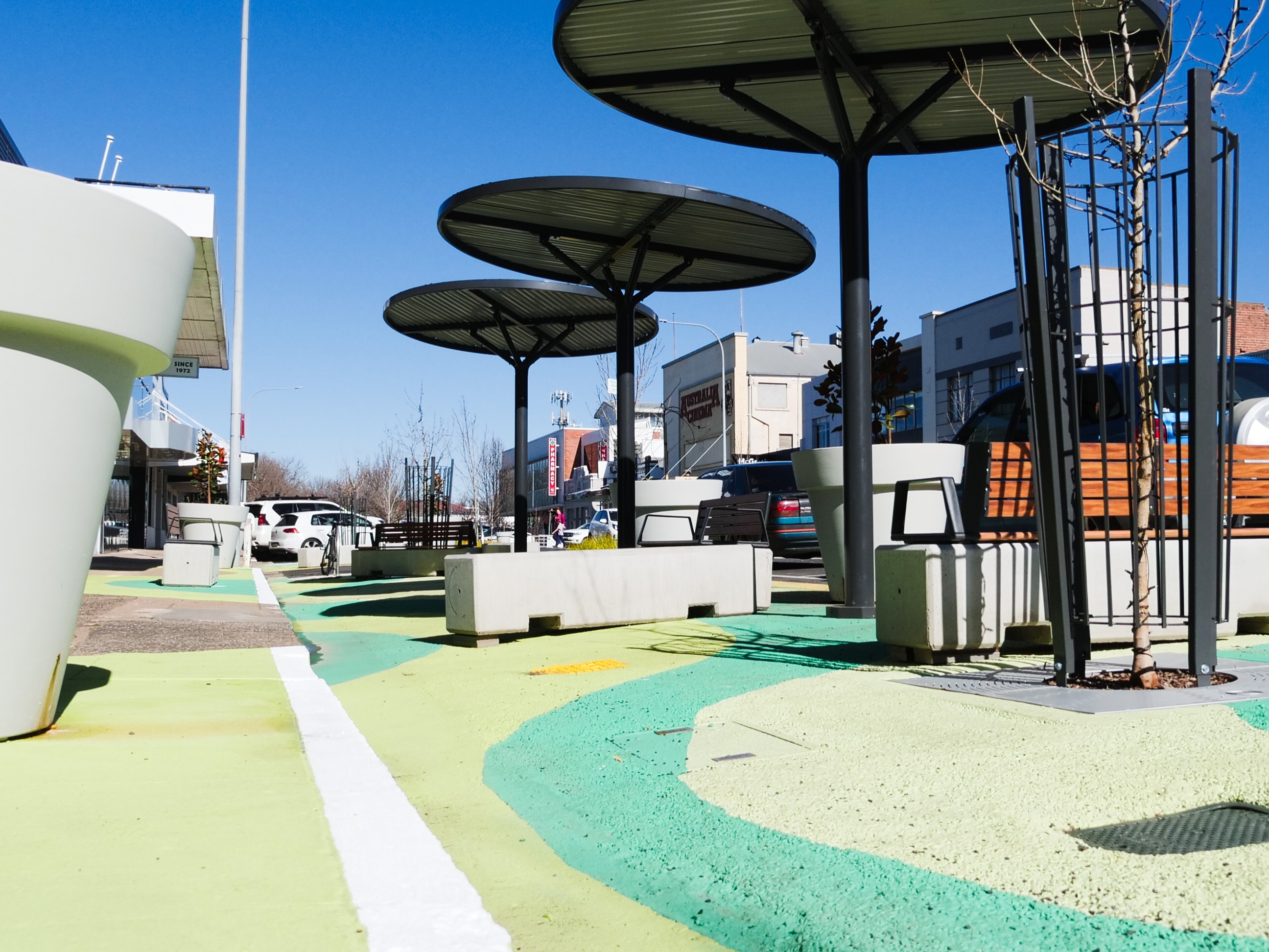 A street painted various shades of green with concrete benches and large metal shade structures.