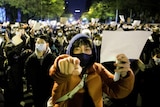 晚上，一群人聚集在一起，其中一些人戴着口罩，举着白纸抗议