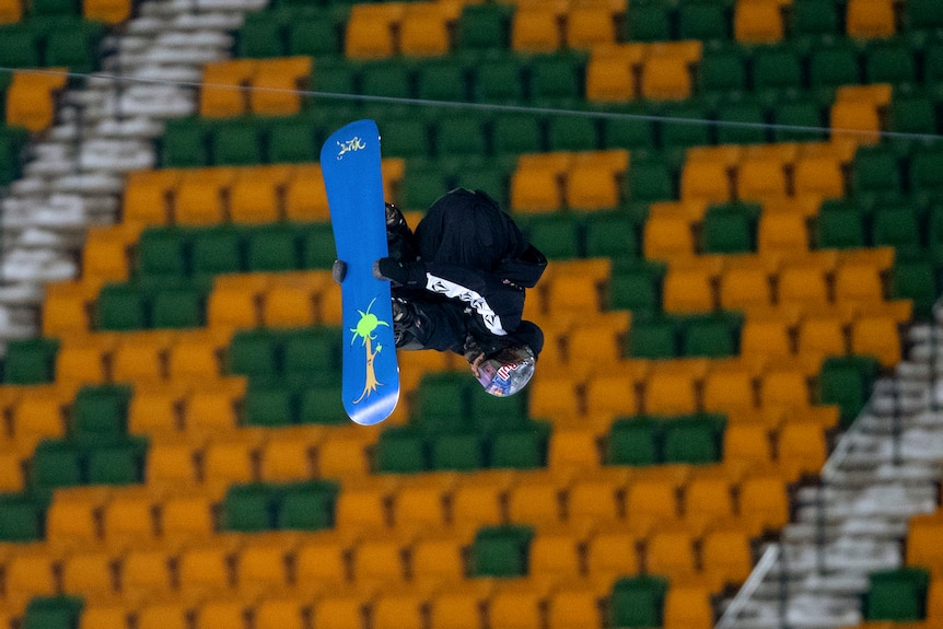 Valentino Guseli sostiene su snowboard boca abajo en un estadio