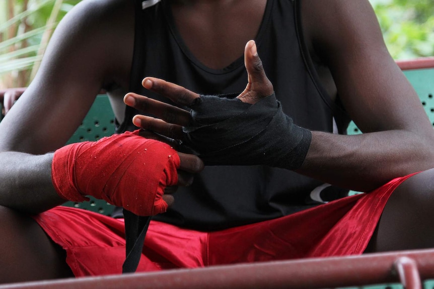 A photo of an Indigenous boxer applying boxing tape to his hands.