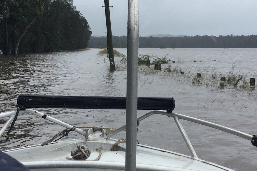 The view from the front of a boat, looking over floodwater and submerged fence lines.
