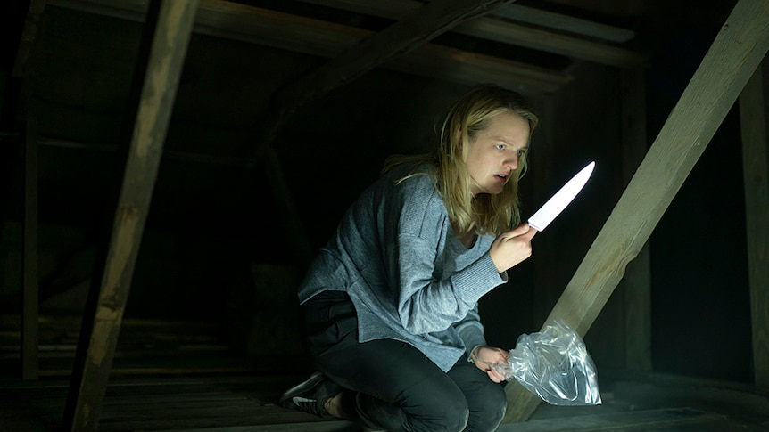 A woman with blonde hair and scared expression crouches in dark attic holds a plastic bag and knife in either hand.