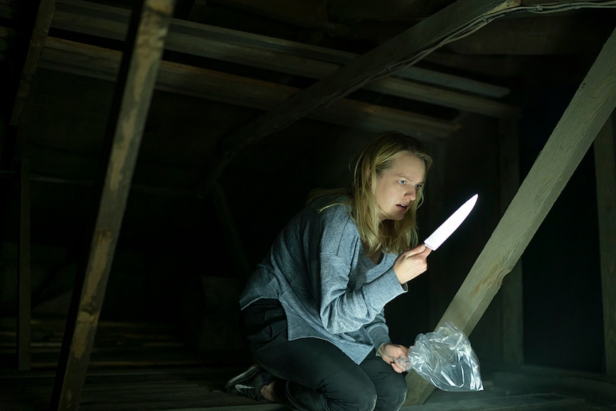 A woman with blonde hair and scared expression crouches in dark attic holds a plastic bag and knife in either hand.