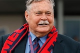 Ron Barassi smiles wearing a suit and a Melbourne Football Club scarf and lanyard