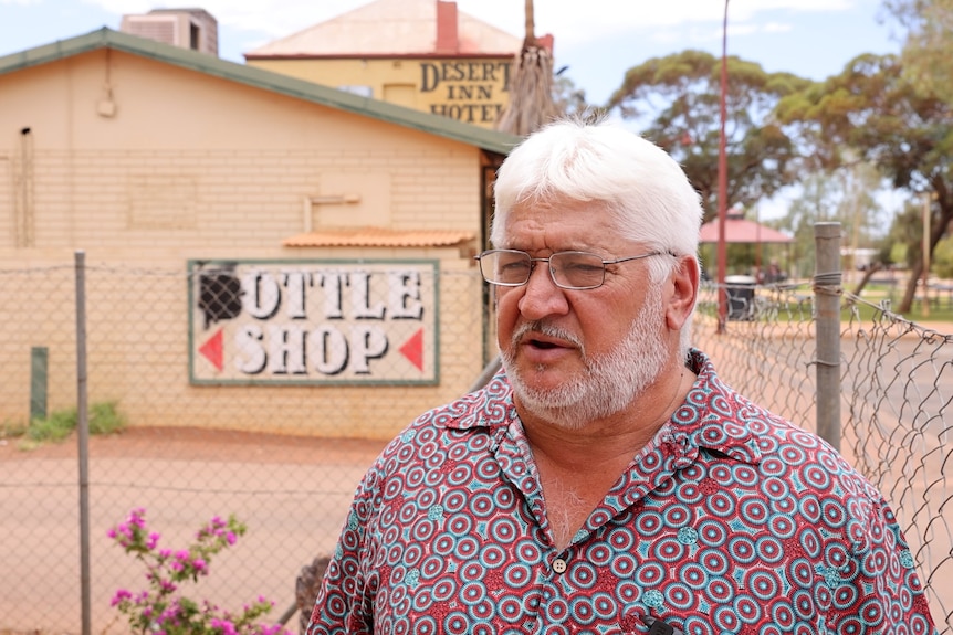 A man standing in front of a bottle shop sign.  