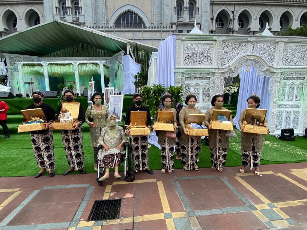 Nine people from the wedding party stand in a row with boxes and wearing masks.