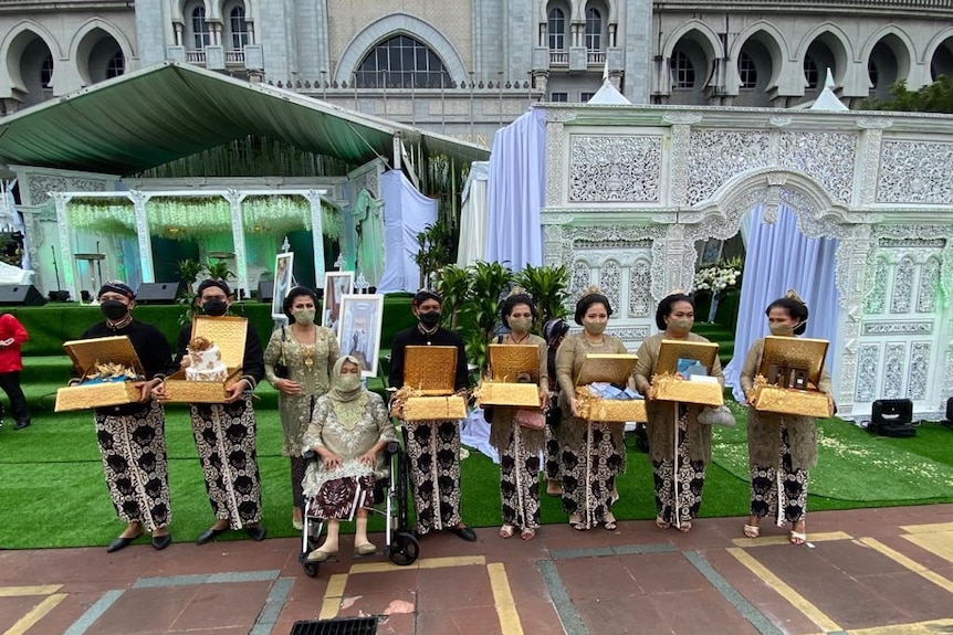 Nine people from the wedding party stand in a row with boxes, wearing masks.