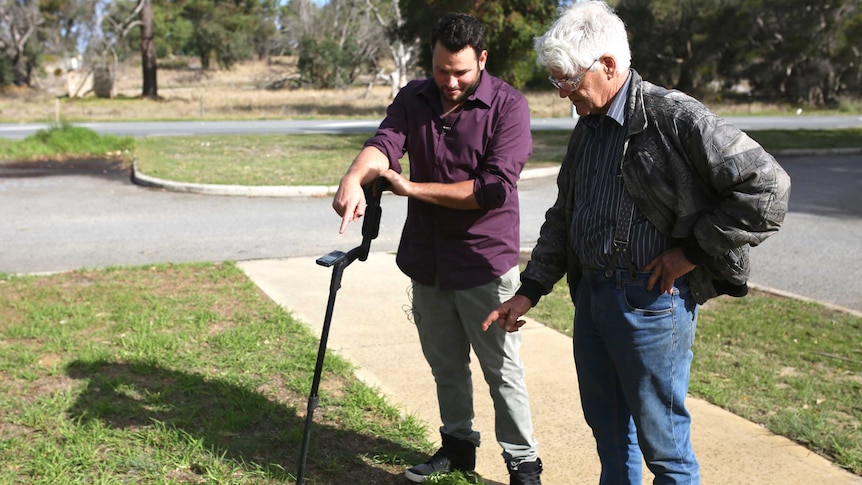 Two men with a metal detector on a patch of grass.