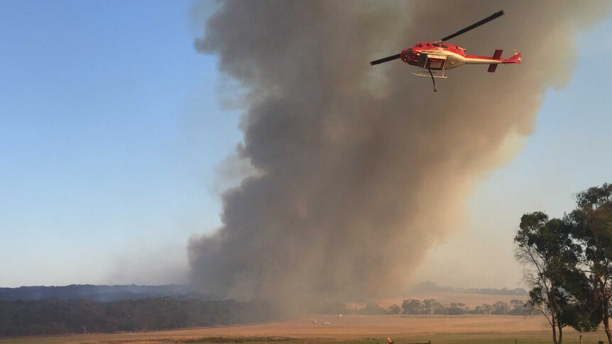 A chopper flies in front of a plume of smoke.