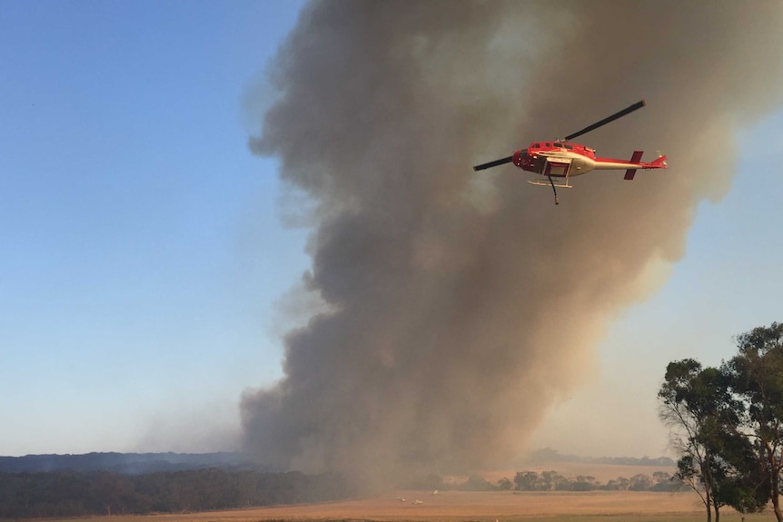 A chopper flies in front of a plume of smoke.