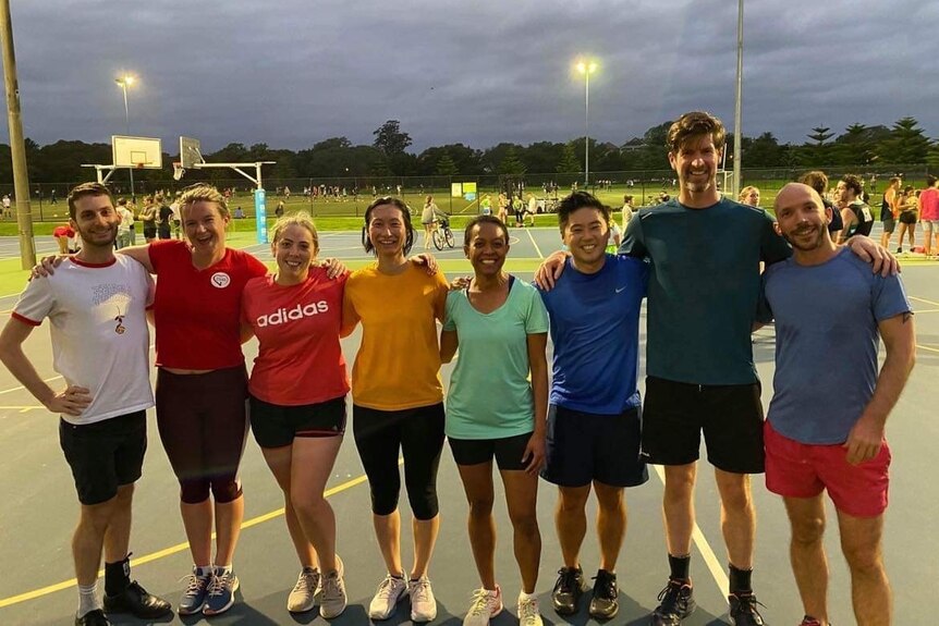 Players wearing different colours of the rainbow pose for a photo at netball courts